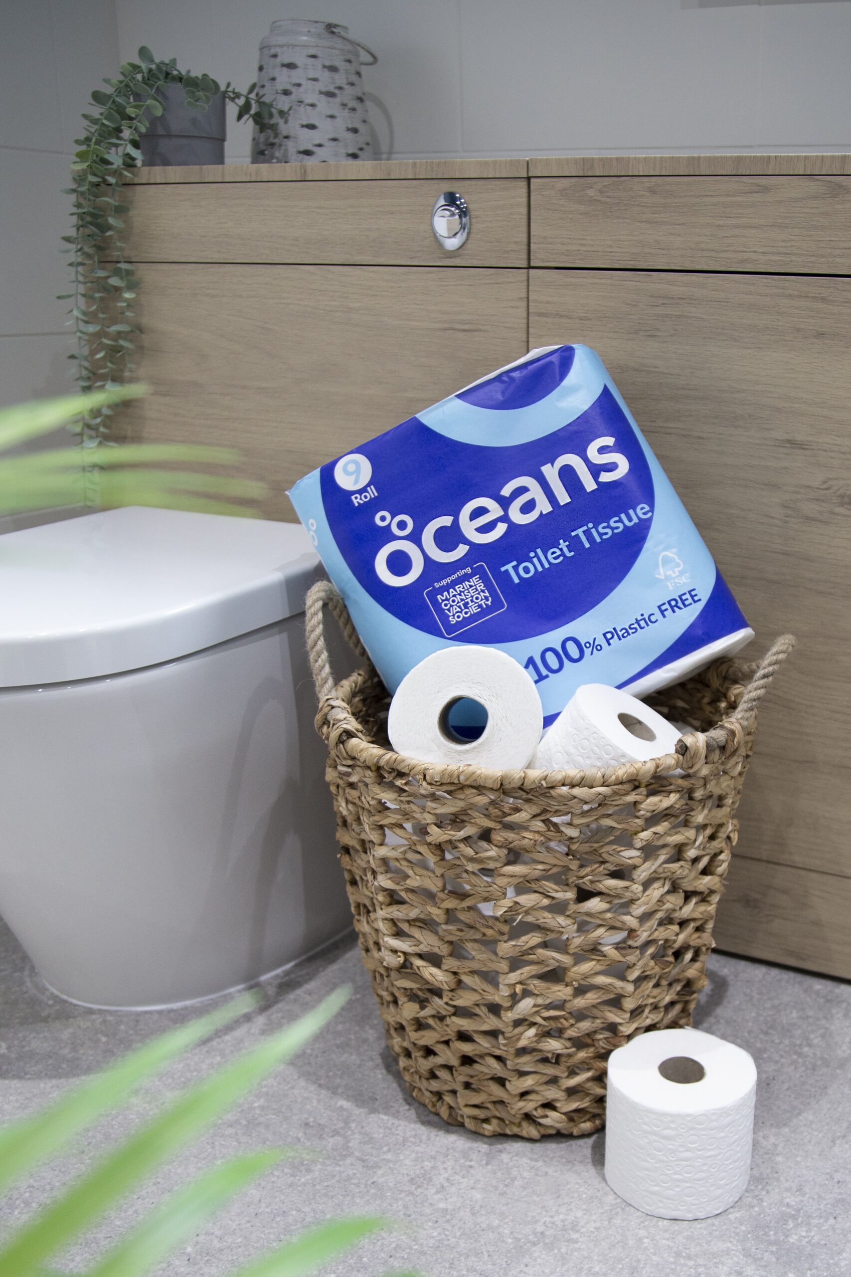 9-pack of Oceans toilet paper in plastic-free packaging inside a basket next to the toilet