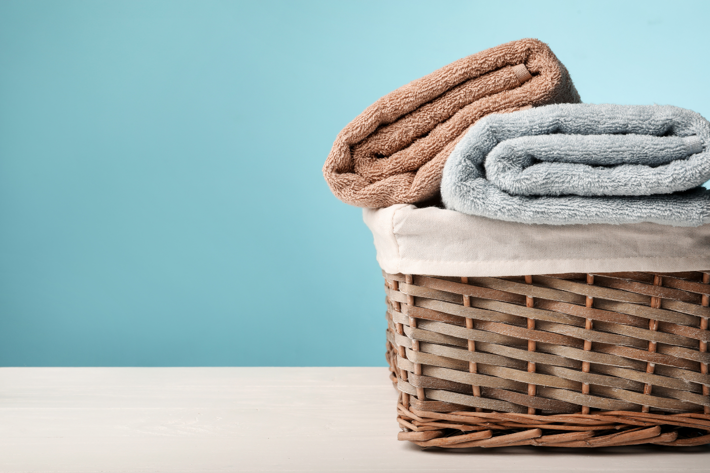 Wicker laundry basket with folded laundry on blue background