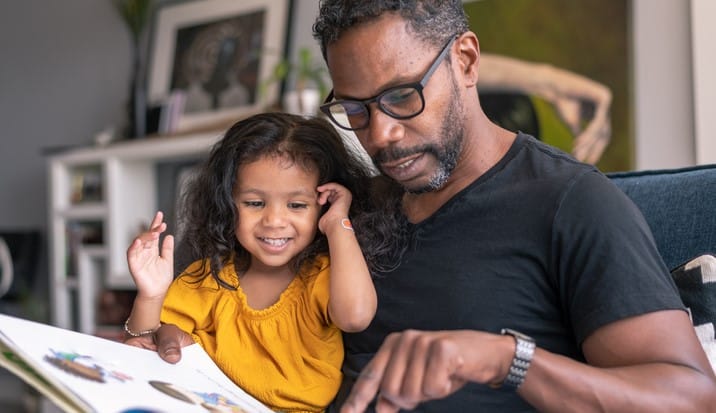 a man teaches his daughter with the help of a picture book.