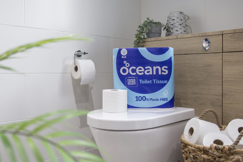 9-pack of Oceans eco toilet roll on top of a toilet surrounded by additional rolls in a basket and on the toilet roll holder
